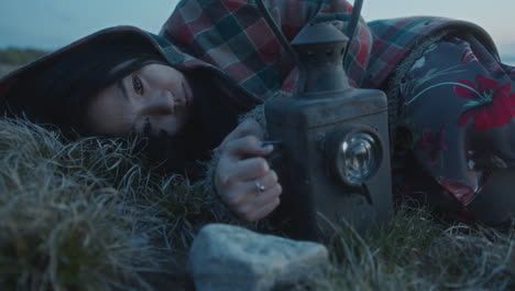 pensive woman lying in field at dusk, staring at flickering lantern