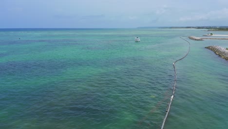 Scenic-summer-flight-above-turquoise-ocean-sea-towards-single-anchored-motor-boat-in-water-on-sunny-day,-Cap-Cana,-Dominican-Republic,-overhead-aerial-approach