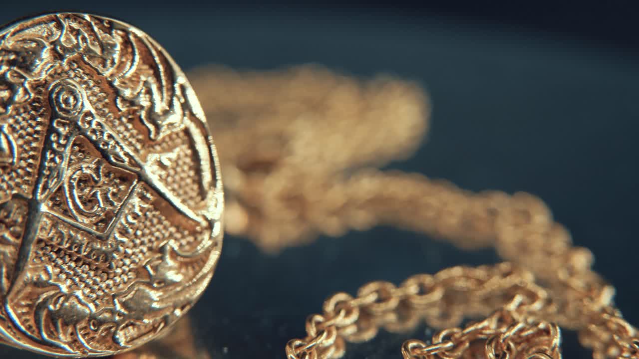 A macro detailed shot of a golden textured freemasons ring, on a mirror reflection stand, illuminati symbol, studio light, 4K video, pan right movement, occultism, necklace shallow depth of field