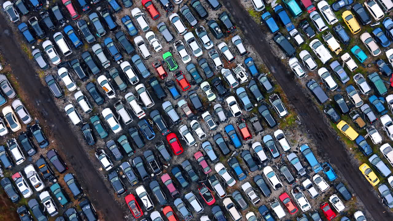 Diagonalt luftfoto af beskadigede biler på en skrotplads. Faktuel droneoptagelse af rækker af gamle køretøjer på et bilophugningsanlæg til udvinding af reservedele.
