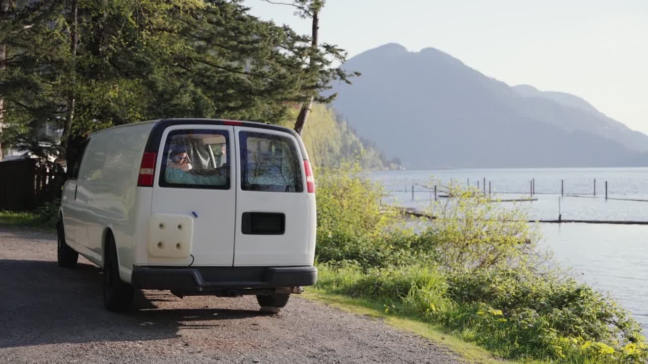 Camper parcheggiato sulla riva di un lago con montagne sullo sfondo, godendosi la vita all'aria aperta