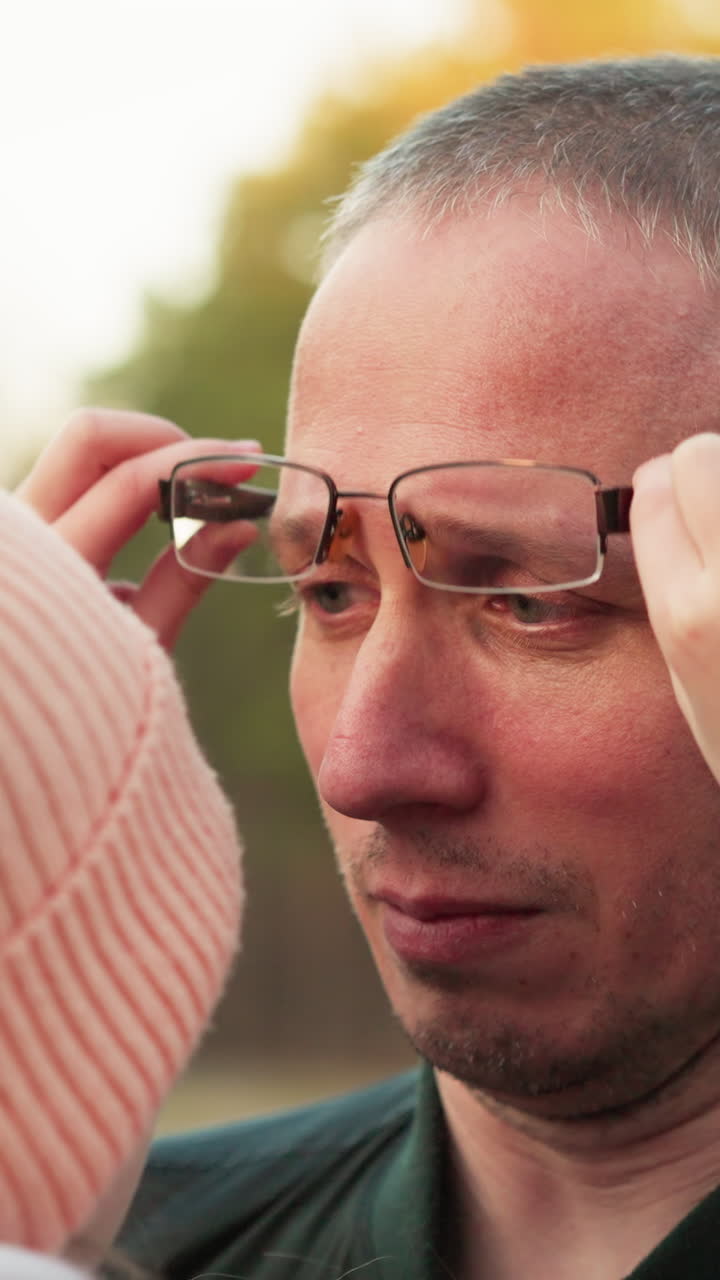 una escena conmovedora donde una niña con un gorro rosado y una chaqueta ajusta las gafas de su padre, mostrando un tierno momento de cuidado y conexión entre ellos. el hombre, con una chaqueta verde