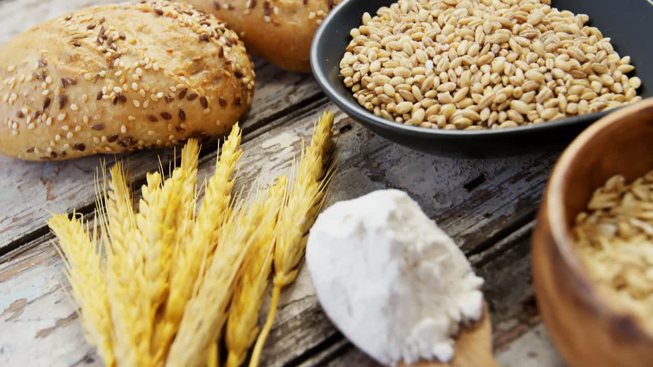 Wheat grains with bread buns, oats and spoon full of flour