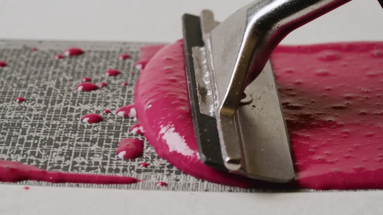 Dråper berører en metallnal som trekkes over en teksturert stripe, og skaper en jevn rosa stripe.