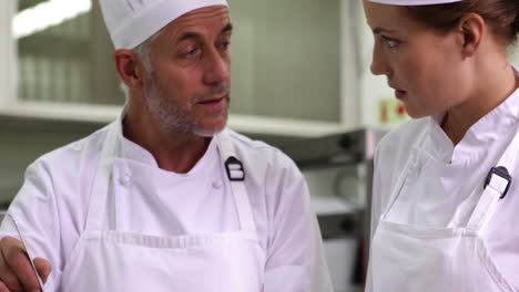 Chef-showing-colleague-content-of-pot-then-smiling-at-camera