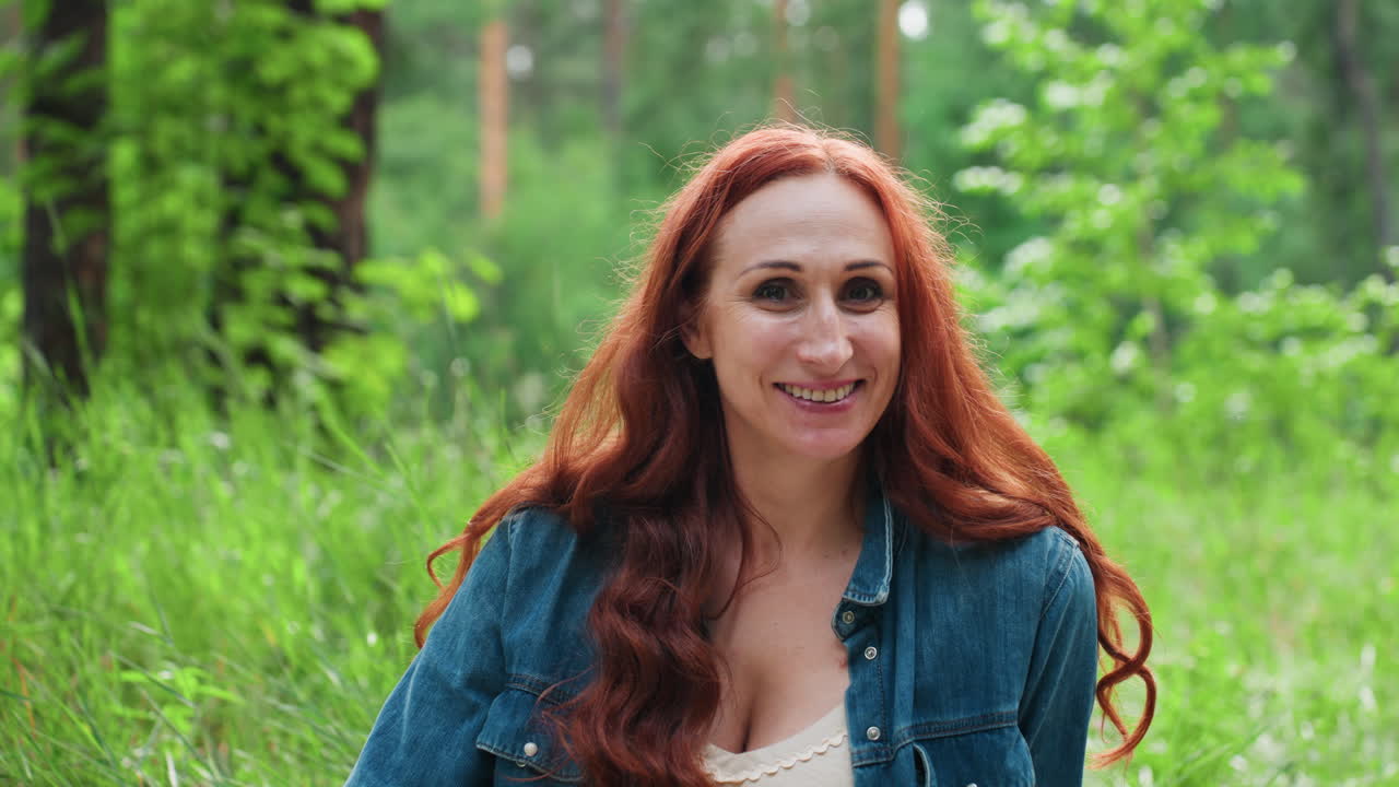 푸르른 자연으로 둘러싸여 평화로운 야외에서 편안하게 풀밭에 앉아 밝게 웃으며 즐거운 시간을 보내는 피크닉을 좋아하는 사람의 인물 사진. 편안한 분위기, 햇빛, 따뜻한 미소가 담겨 있어요.