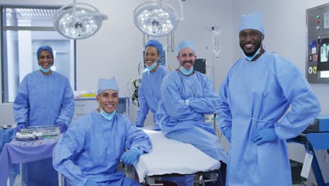 diversos médicos masculinos y femeninos con máscaras faciales de pie en el quirófano sonriendo a la cámara