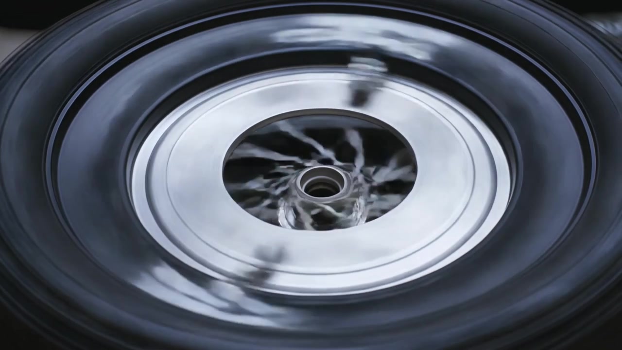 Spinning vehicle wheel and polished hubcap rotating in garage bay, fragments moving clockwise