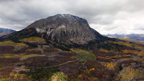 dramatic cloudy autumn aspen tree fall colors kebler pass trailhead aerial cinematic drone snow on peaks landscape crested butte gunnison colorado early fall red yellow orange rocky mountains backward