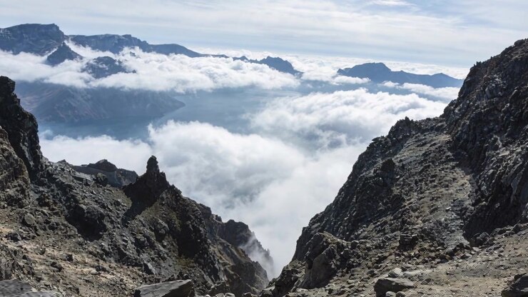 Banco di nuvole in movimento spinto dal vento attraverso una stretta fessura in un passo di montagna elevato, incorniciando creste rocciose.