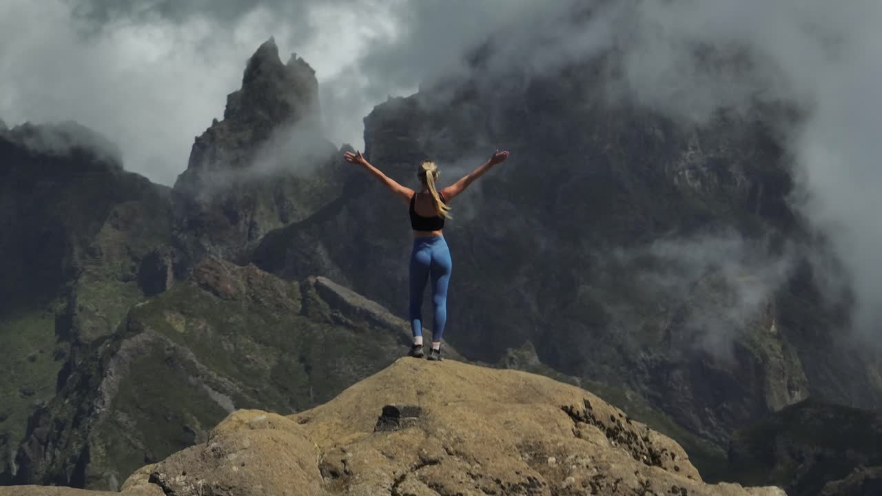 mujer en forma de pie en el pico de la montaña con las manos en el aire de la felicidad, paisaje dramático