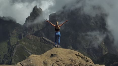 fit woman standing on mountain peak with hands in air from happiness, dramatic landscape