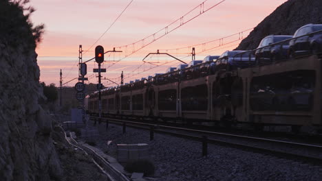 cargo train carrying new cars passes on railroad track during early sunrise