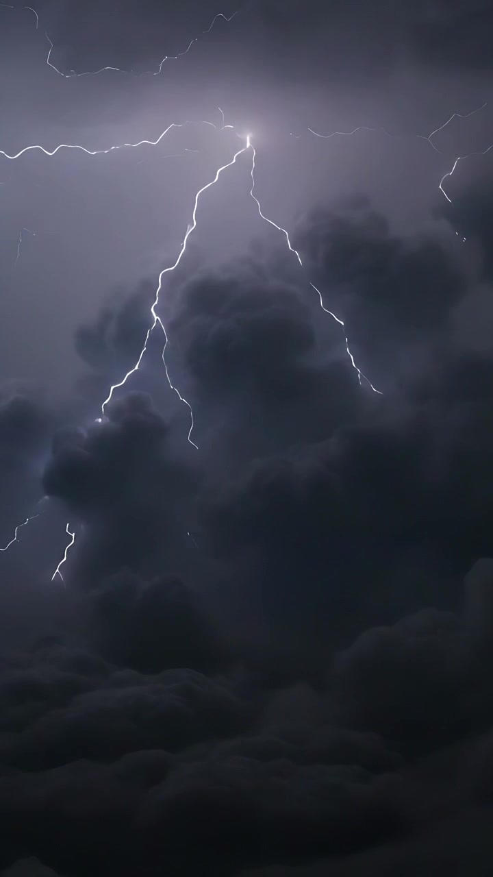 Video verticale: Grande nuvola temporalesca che pulsa nel cielo notturno con cime illuminate, caricando ed emettendo fulmini.