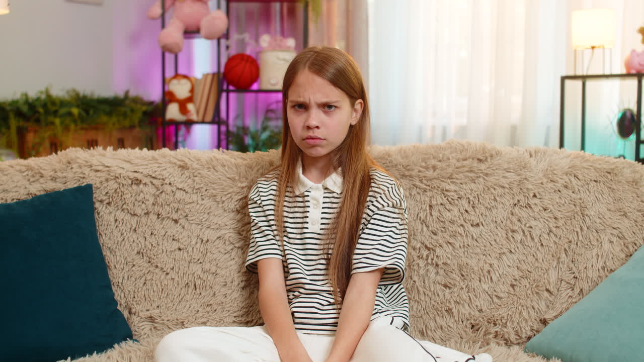 Child girl kid crosses arms in anger sitting on sofa expressing frustration dissatisfaction at home