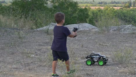 slow motion of caucasian kid playing with his rc car toy in the fields, moving backwards