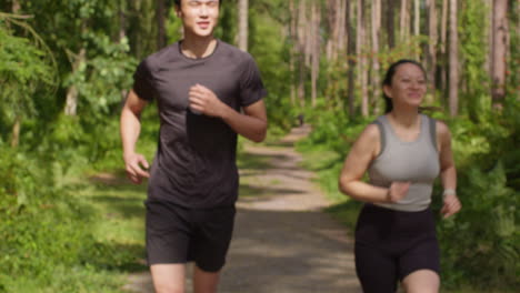 mid adult couple exercising doing work out outdoors running along track through forest towards camera wearing sports clothing 2