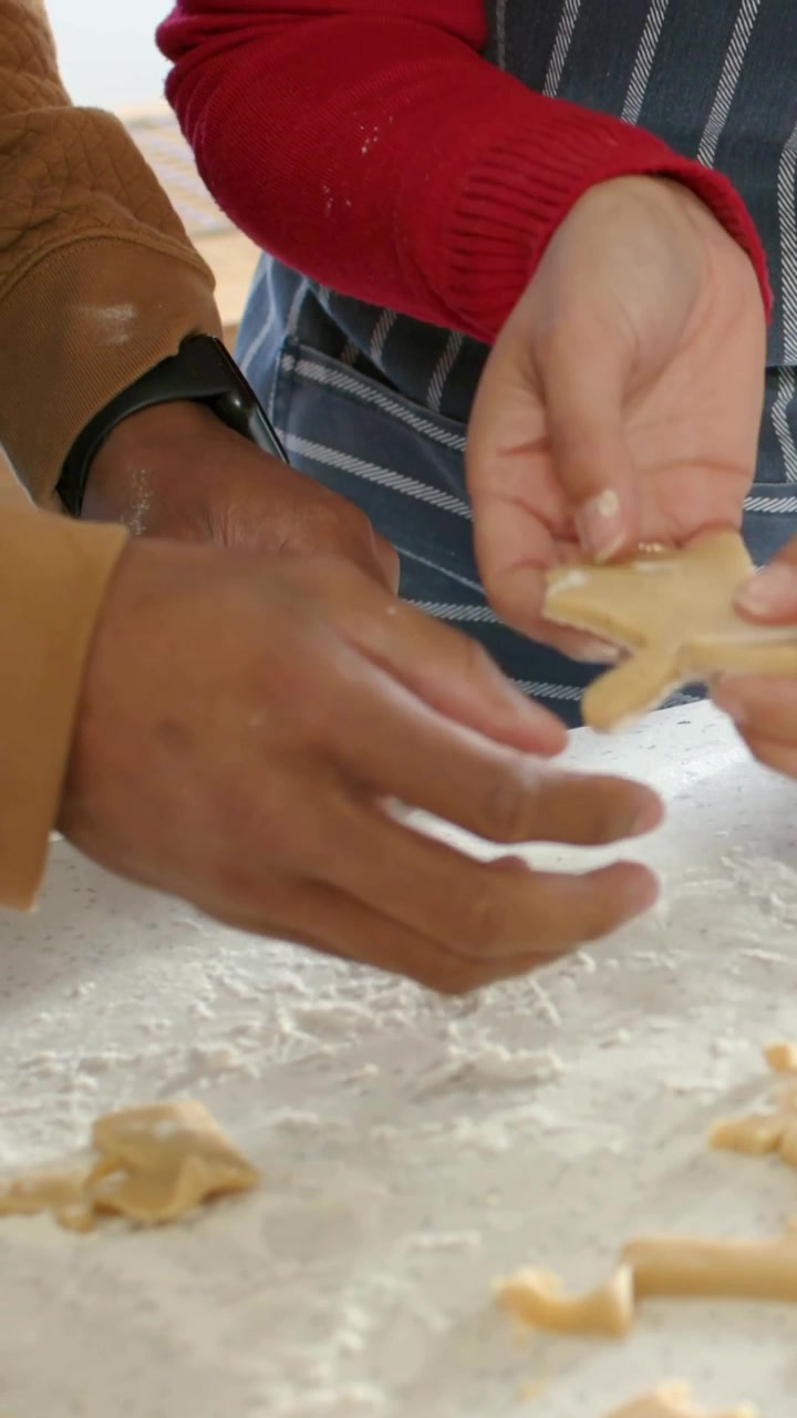 Vertical video: Pressing cutters into dough, apron-clad hands lifting cookies on counter for baking