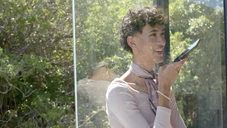 smiling and talking on smartphone, non binary person standing by window at home