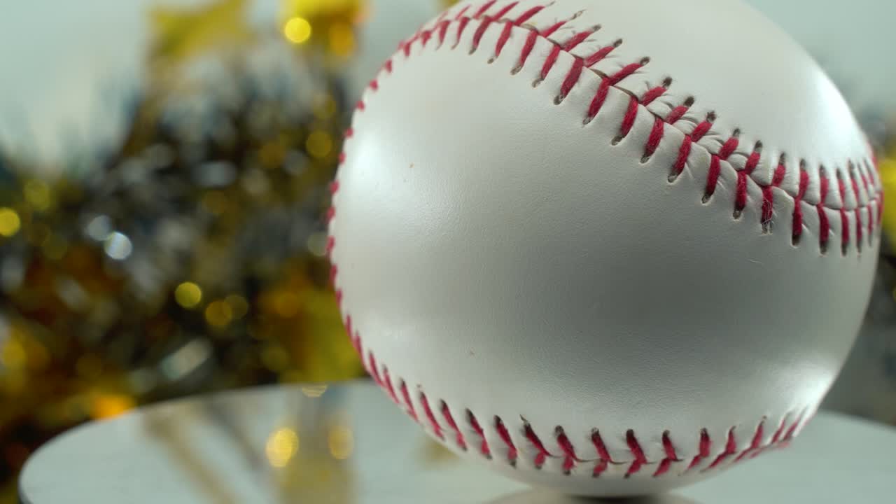 cámara cinematográfica lenta de primer plano de una pelota de base blanca, puntos rojos de béisbol en un soporte brillante, decoraciones de navidad borrosas en el fondo, iluminación de estudio profesional, panela de video 4k a la derecha