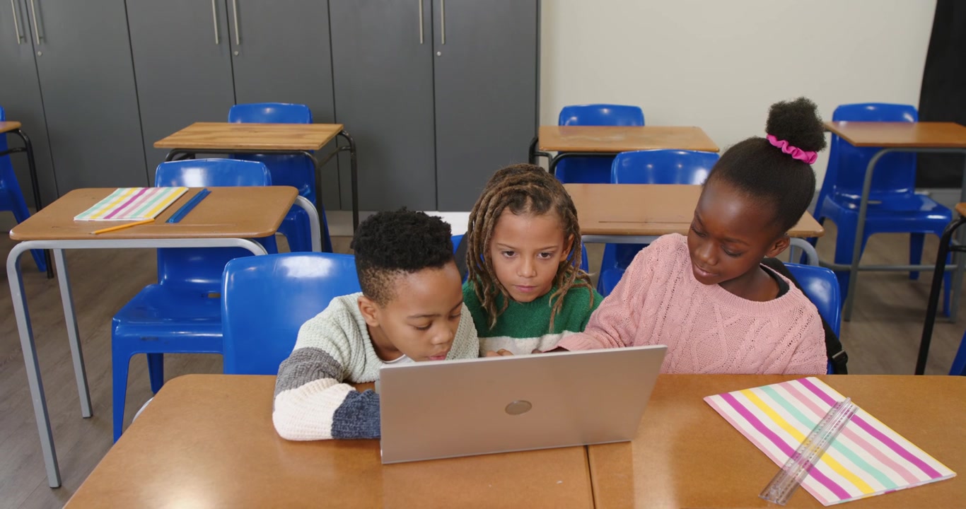 Adolescenti afroamericani che si chinano e indicano un laptop argentato in classe, mentre lavorano a un compito.