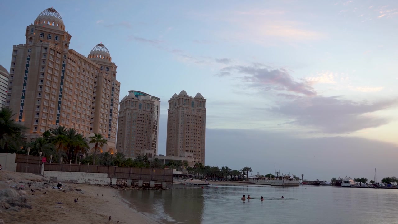 Splendida vista all'alba di persone che nuotano nelle calme acque del Golfo Persico, proprio accanto a un lussuoso resort alberghiero a cupola a Doha, Qatar.