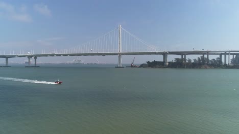 Toma-Aérea-De-Vehículos-Moviéndose-En-El-Puente-De-La-Bahía-De-San-Francisco–oakland-Con-La-Ciudad-Al-Fondo