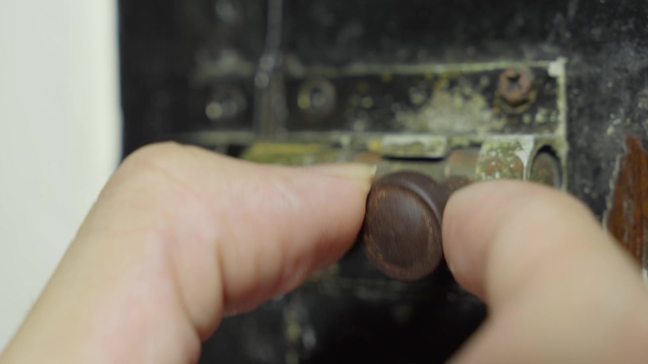 Hand turning a rusty old door lock with visible wear and tear, close-up