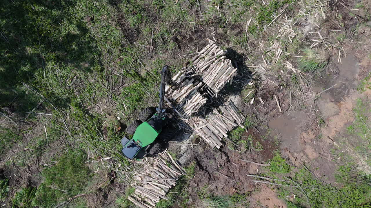 Top down aerial view over the logging operation with heavy machine stacking logs in a partially cleared forest area.