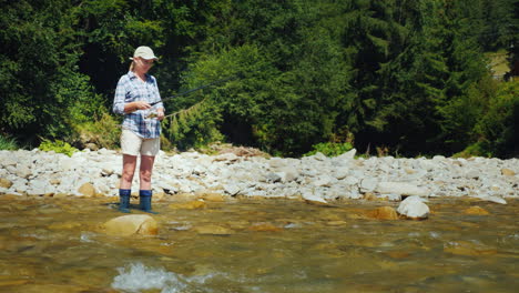 vacaciones de verano activas - una mujer está pescando cerca de la orilla de un río de montaña