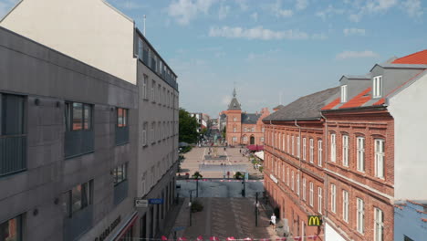 Forward-slow-flight-through-Torvegade-street-in-Esbjerg,-Denmark.-Aerial-Dolly-over-the-famous-Torvet-square-with-brick-buildings-and-the-statue-of-Christian-IX