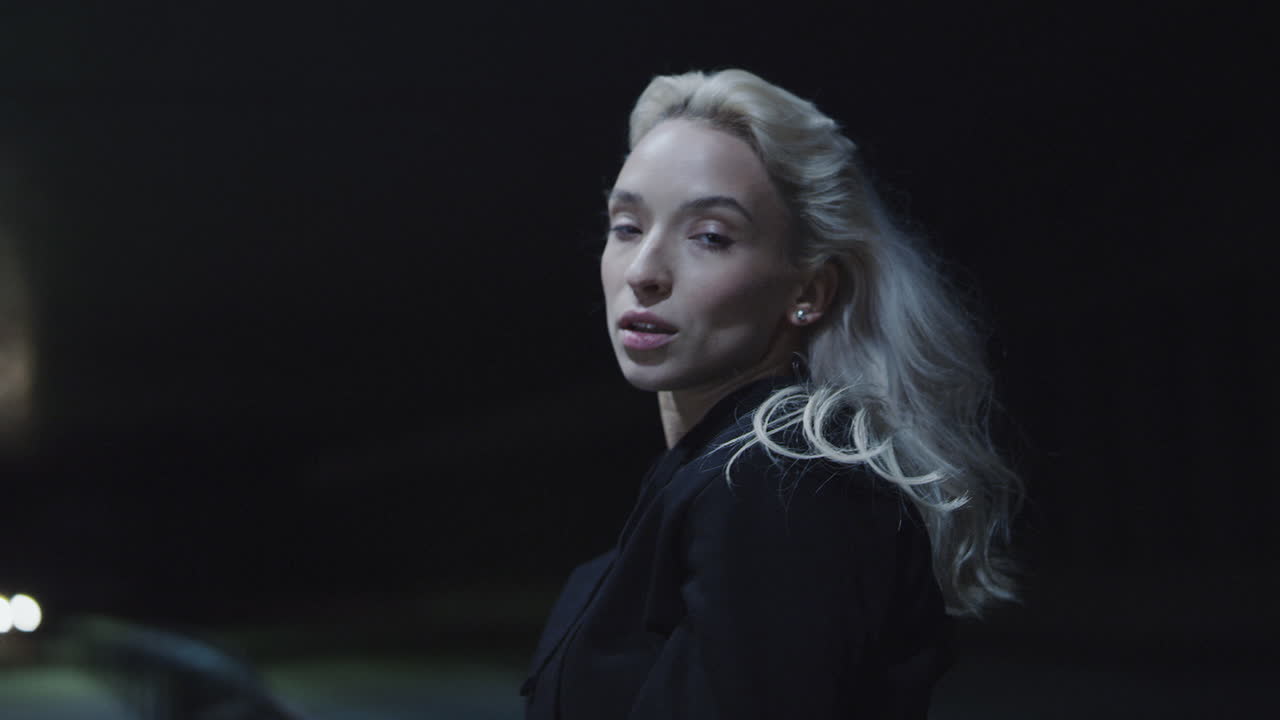Modelo feminina tocando o cabelo em área urbana à noite, sob as luzes da cidade.