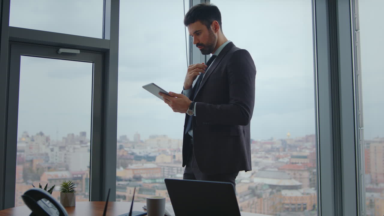 gestore concentrato guardando schermo tablet in piedi ufficio moderno. uomo che lavora al pad