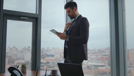 gerente focado olhando tela de tablet de pé escritório moderno. homem trabalhando em pad