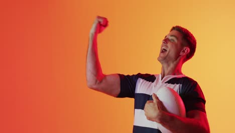 Happy-caucasian-male-rugby-player-raising-hands-over-orange-lighting