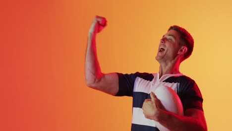 feliz jugador de rugby masculino caucásico levantando las manos sobre la iluminación naranja