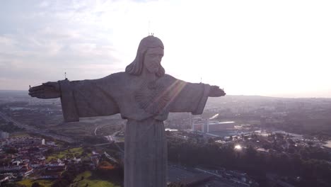 drone descendiendo lentamente con la estatua cristo rei de jesucristo frente al sol poniente en portugal lisboa