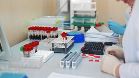 young female nurse puts blood samples in tubes into a special rack on a table. close up hands in protective gloves of female laboratory technicians working with test tubes in a laboratory.