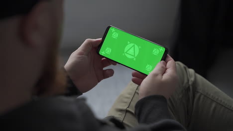 man holding smartphone with horizontal green screen chroma, swiping and scrolling. mockup.