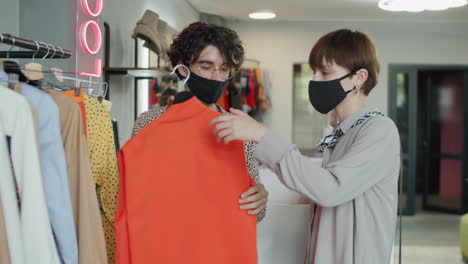 Friends-in-Face-Masks-Choosing-Garment-in-Clothes-Shop