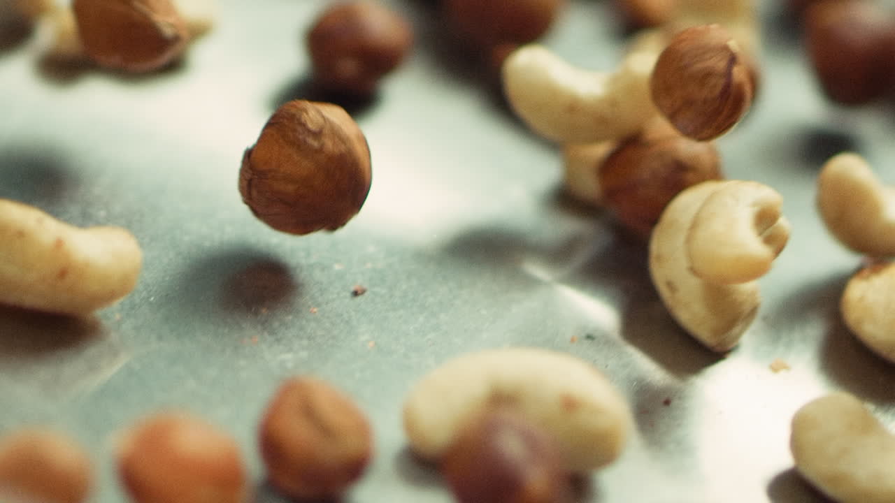 Closeup nuts frying on metal pan in slow motion. Mix of hazel and cashew nuts