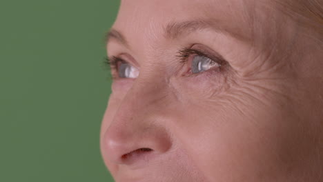 close up view of half face of blonde mature woman with blue eyes smiling and looking at side on green background