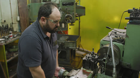 Caucasian-male-factory-worker-at-a-factory-sitting-at-a-workbench-and-operating-machinery