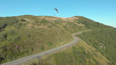 Paraglider-soars-over-mountain-road-at-sunset