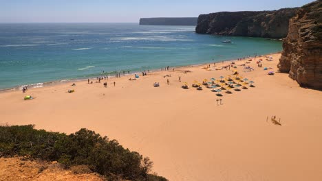 Clifftop-view-panorama-of-the-perfect-beach-near-Capo-de-Vincent-on-a-hot-sunny-day-showing-black-cliffs-and-a-moored-yacht-in-the-bay