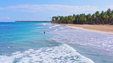 aerial drone view passing a man fishing in waves, at the playa coson beach, in dominican republic