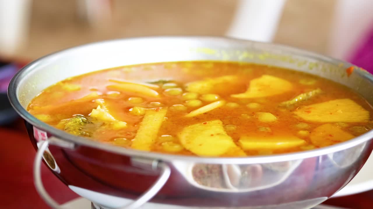 A close-up view of a vibrant yellow curry with vegetables in a stainless steel pot.