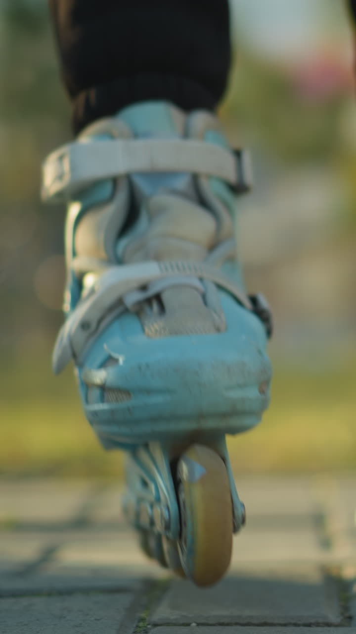 A close-up shot of a person sitting on a park bench, fastening the straps of a rollerblade on one foot while the other foot is already in a rollerblade. The person is not fully visible