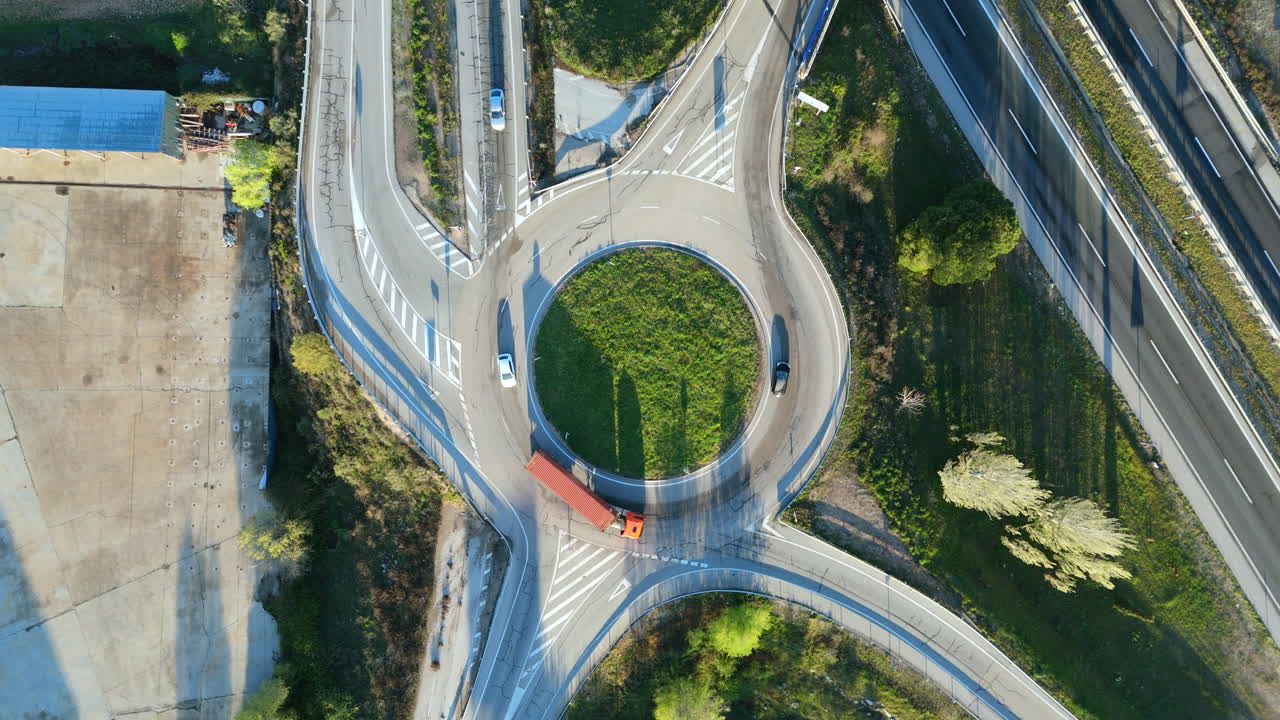 Drone top down shot of a circular road junction with cars and a truck entering the roundabout. Symmetrical urban planning concept. Ideal for traffic, transport, logistics and infrastructure themes
