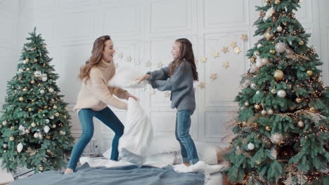 Smiling-mother-and-daughter-playing-with-pillows-in-luxury-bedroom.